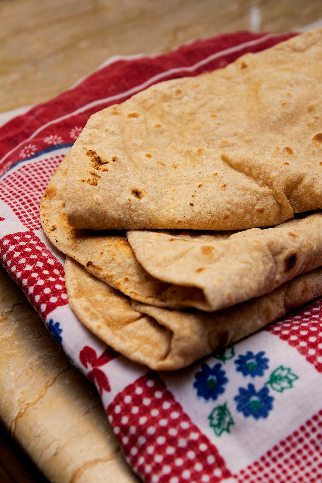 Soft whole wheat rotis folded and stacked on a red and white checkered cloth