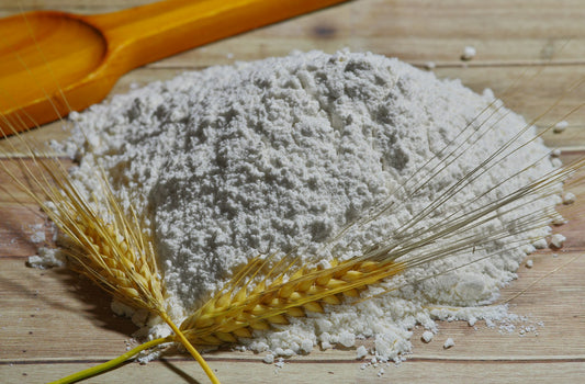 Pile of wheat flour with wheat stalks laid on top, on a wooden kitchen surface